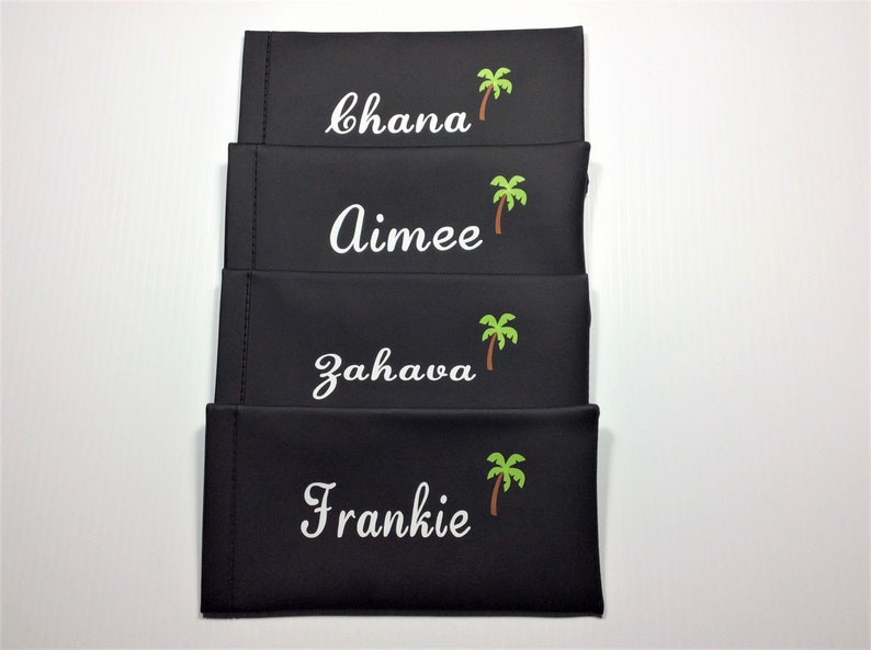 May include: Four black eyeglass cases with white embroidered names and green palm tree designs. The names are "Chana", "Aimee", "Zahava", and "Frankie".