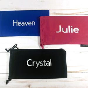 May include: Three drawstring bags with different names embroidered on them. The bags are blue, pink, and black.