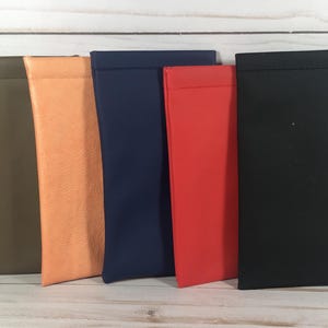 Op de afbeelding: Vijf rechthoekige etuis op een rij, met een gladde, matte afwerking. De kleuren van links naar rechts zijn olijfgroen, licht perzik, marineblauw, felrood en effen zwart. Elk etui heeft een eenvoudig ontwerp met strakke lijnen.