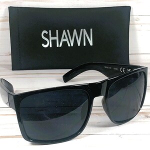 Puede incluir: Gafas de sol negras con montura rectangular y lentes oscuras. Las gafas de sol est&aacute;n junto a un estuche negro con el nombre "SHAWN" impreso en plata. Las gafas tienen una marca CE y UK.