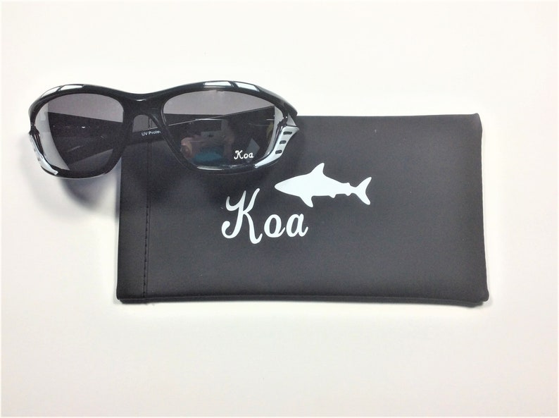 May include: Black sunglasses with white accents and a black case with a white shark and the word "Kao" printed on it.