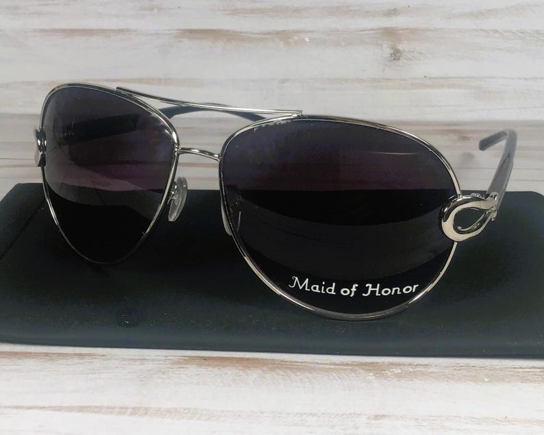 May include: Silver aviator sunglasses with dark lenses. The sunglasses have a decorative silver accent on the temples and the text "Maid of Honor" on the lens.