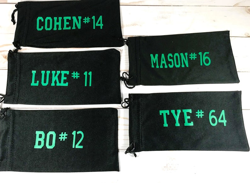 May include: Black drawstring pouches with green text. The pouches display names and numbers: COHEN #14, LUKE #11, BO #12, MASON #16, and TYE #64. Each pouch has a black drawstring closure.
