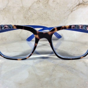 May include: Eyeglasses with a tortoiseshell pattern frame and blue accents. The top of the frame is embellished with pink and blue rhinestones. The lenses are clear. The glasses are designed for vision correction.