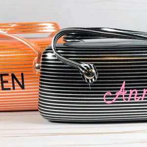 May include: Two striped cosmetic bags. One is orange with the name "OWEN" in black. The other is black and white with the name "Anna" in pink. Both bags have a handle and silver hardware.