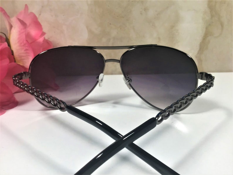 Peut inclure: Lunettes de soleil aviateur noires avec un d&eacute;tail de cha&icirc;ne sur les branches. Les verres sont d&eacute;grad&eacute;s, passant du fonc&eacute; au clair.