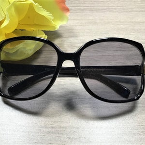 May include: Black oversized sunglasses with a dark gray lens. The sunglasses have a rounded square shape.