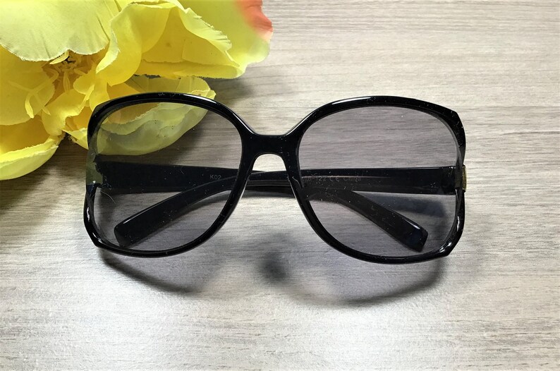 May include: Black oversized sunglasses with a dark gray lens. The sunglasses have a rounded square shape.