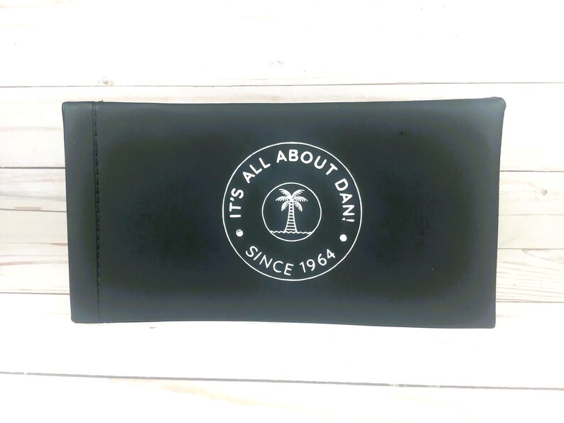 May include: Black zippered pouch with a white circle logo that says "It's All About Dan! Since 1964" and a palm tree inside the circle.