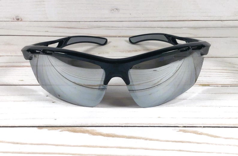 May include: Sport sunglasses featuring a glossy black frame and reflective silver mirrored lenses. The eyewear has a wrap-around design with vented temples and a contoured bridge, providing a wide field of vision and a secure fit for active use.