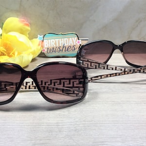 Peut inclure: Deux paires de lunettes de soleil brunes avec un motif g&eacute;om&eacute;trique sur les branches et des verres bruns. Les lunettes de soleil sont sur une surface en bois brun clair.