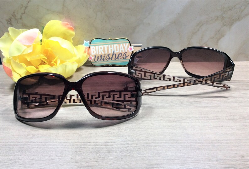 Peut inclure: Deux paires de lunettes de soleil brunes avec un motif g&eacute;om&eacute;trique sur les branches et des verres bruns. Les lunettes de soleil sont sur une surface en bois brun clair.