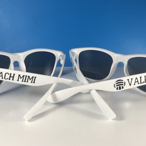 May include: Two pairs of white sunglasses with black lenses. One pair has the text "COACH MIMI" on the arm and the other pair has the text "VALKYRIE" and a volleyball icon on the arm.