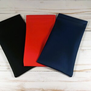 Puede incluir: Tres estuches para gafas en negro, rojo y azul marino se muestran sobre una superficie de madera clara. Los estuches son rectangulares, con una textura suave y lisa, y est&aacute;n ligeramente inclinados hacia el espectador.