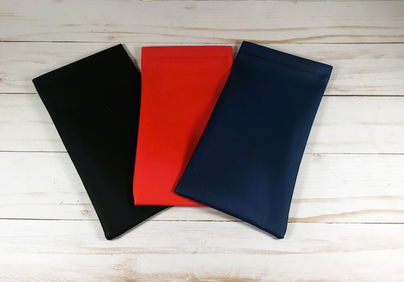 Puede incluir: Tres estuches para gafas en negro, rojo y azul marino se muestran sobre una superficie de madera clara. Los estuches son rectangulares, con una textura suave y lisa, y est&aacute;n ligeramente inclinados hacia el espectador.