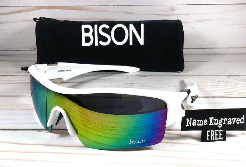 May include: White sports sunglasses with a rainbow iridescent lens. The sunglasses have a black case with the word "BISON" printed on it. A white sign says "Name Engraved FREE".