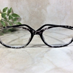Peut inclure: Lunettes avec une monture au motif mouchet&eacute; noir et blanc. Les coins ext&eacute;rieurs de la monture sont orn&eacute;s de petits clous m&eacute;talliques dor&eacute;s. Les branches sont enti&egrave;rement noires et les verres sont clairs et transparents.