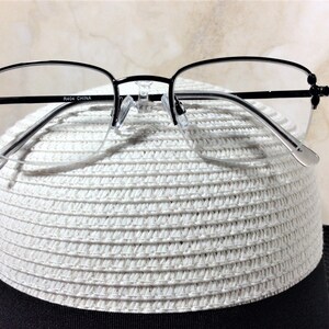 May include: Black half-rim eyeglasses with clear lenses rest on a white woven hat with a black brim. The glasses have a delicate design with small decorative elements on the temples. The text "R404 CHINA" is printed on the frame.