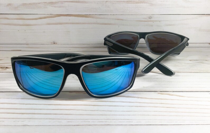 K&ouml;nnte beinhalten: Zwei Sonnenbrillen, eine mit blauen verspiegelten Gl&auml;sern und eine mit dunklen Gl&auml;sern. Beide Brillen haben schwarze Rahmen.