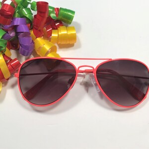 May include: A pair of red aviator sunglasses with dark lenses. The sunglasses are on a white background.