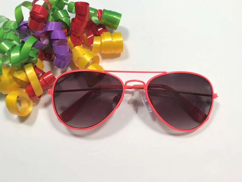 May include: A pair of red aviator sunglasses with dark lenses. The sunglasses are on a white background.