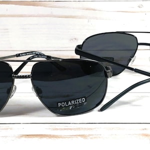 May include: Two pairs of black aviator sunglasses with polarized lenses. The sunglasses have a silver metal frame.
