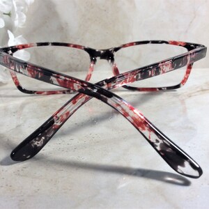 Pu&ograve; includere: Occhiali rettangolari con montatura marmorizzata rossa, nera e bianca. Le aste sono nere alle estremit&agrave;, fondendosi con il motivo. Le lenti sono trasparenti, per un look moderno.