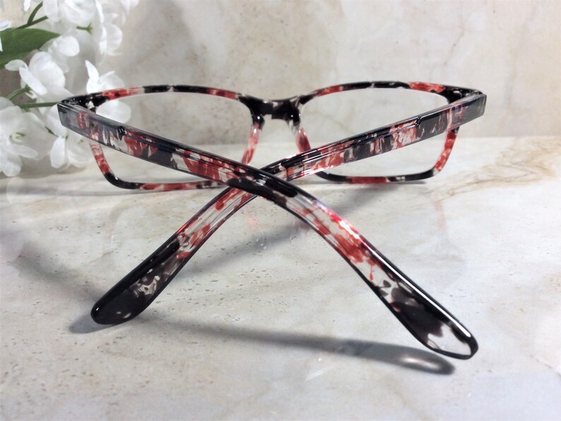 Pu&ograve; includere: Occhiali rettangolari con montatura marmorizzata rossa, nera e bianca. Le aste sono nere alle estremit&agrave;, fondendosi con il motivo. Le lenti sono trasparenti, per un look moderno.
