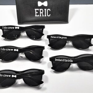May include: Four pairs of black sunglasses with white text on the frames. The text reads "I do crew" with a bowtie symbol, "Father of the groom", and "Brother of the bride".