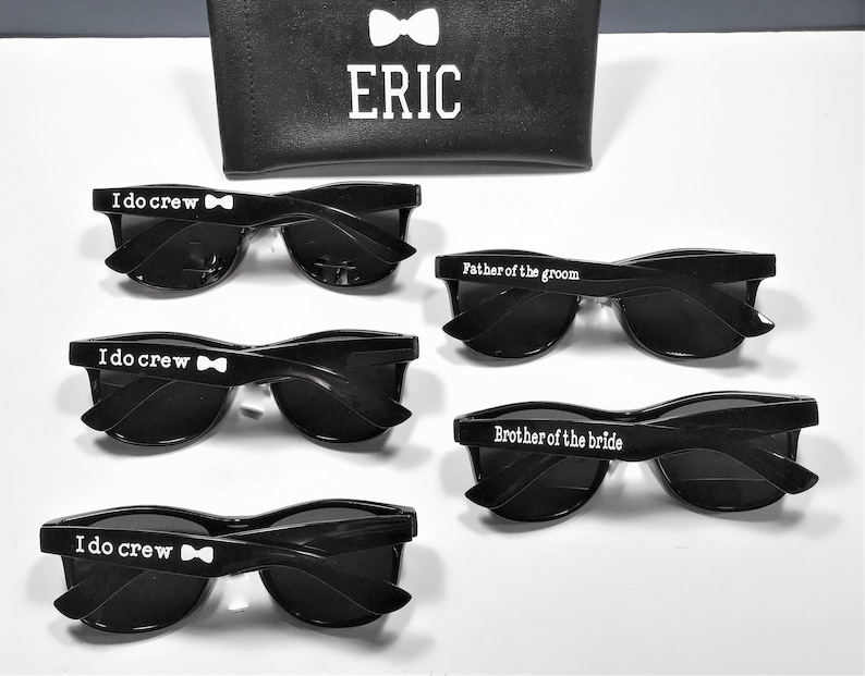 May include: Four pairs of black sunglasses with white text on the frames. The text reads "I do crew" with a bowtie symbol, "Father of the groom", and "Brother of the bride".