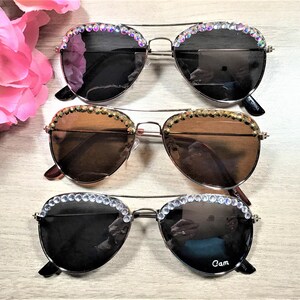 Pu&ograve; includere: Tre paia di occhiali da sole aviator con strass intorno alle montature. Gli occhiali hanno lenti di diversi colori: nero, marrone e marrone chiaro.