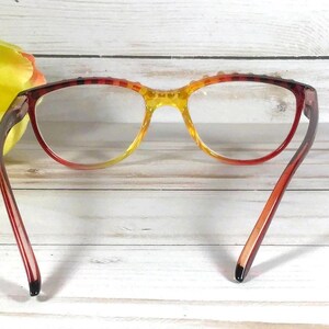 Puede incluir: Gafas con una montura degradada que pasa de un rojo intenso en los bordes exteriores a un amarillo brillante en el puente. Las monturas tienen un acabado transl&uacute;cido e incluyen peque&ntilde;os tachones decorativos a lo largo del borde superior.