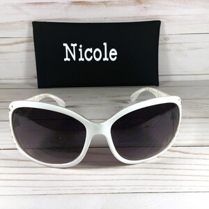 K&ouml;nnte beinhalten: Wei&szlig;e Sonnenbrille mit schwarzem Etui. Das Etui tr&auml;gt den Namen "Nicole" in wei&szlig;er Schrift.
