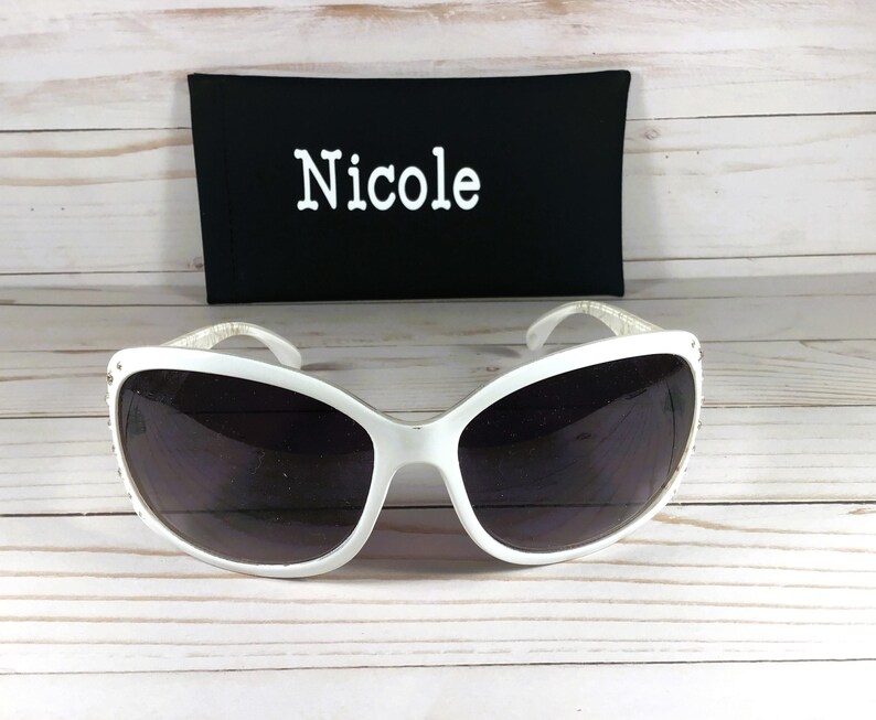 K&ouml;nnte beinhalten: Wei&szlig;e Sonnenbrille mit schwarzem Etui. Das Etui tr&auml;gt den Namen "Nicole" in wei&szlig;er Schrift.