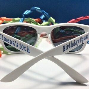 Peut inclure: Lunettes de soleil en plastique blanc avec du texte bleu qui dit "Jimena's 10th Birthday Squad".
