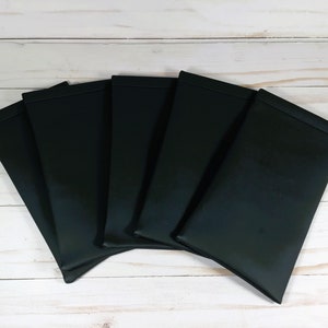 May include: Six black leatherette eyeglass cases arranged in a fan shape on a white wooden surface.