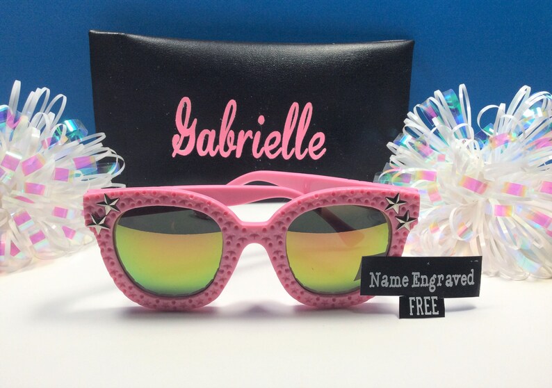 Puede incluir: Gafas de sol rosas con un dise&ntilde;o de estrella en el lateral y lentes de espejo arco&iacute;ris. Las gafas de sol vienen con una funda negra y una etiqueta que dice "Nombre grabado GRATIS".