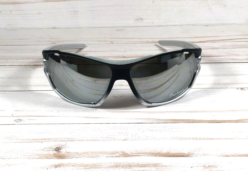 May include: Silver and black sunglasses with mirrored lenses. The sunglasses have a Jackery logo on the right lens.