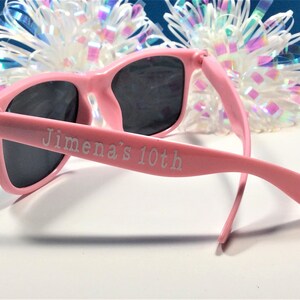 May include: Pink plastic sunglasses with black lenses. The sunglasses have "Jimena's 10th" engraved on the side.