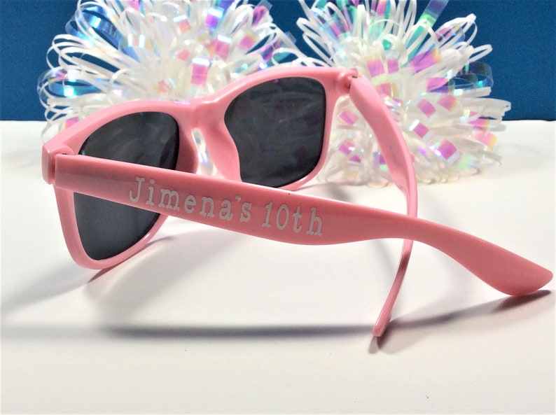 May include: Pink plastic sunglasses with black lenses. The sunglasses have "Jimena's 10th" engraved on the side.