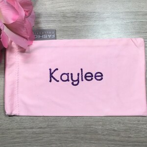May include: Pink fabric eyeglass case with the name "Kaylee" embroidered in purple glitter.