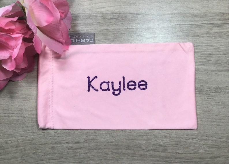 May include: Pink fabric eyeglass case with the name "Kaylee" embroidered in purple glitter.