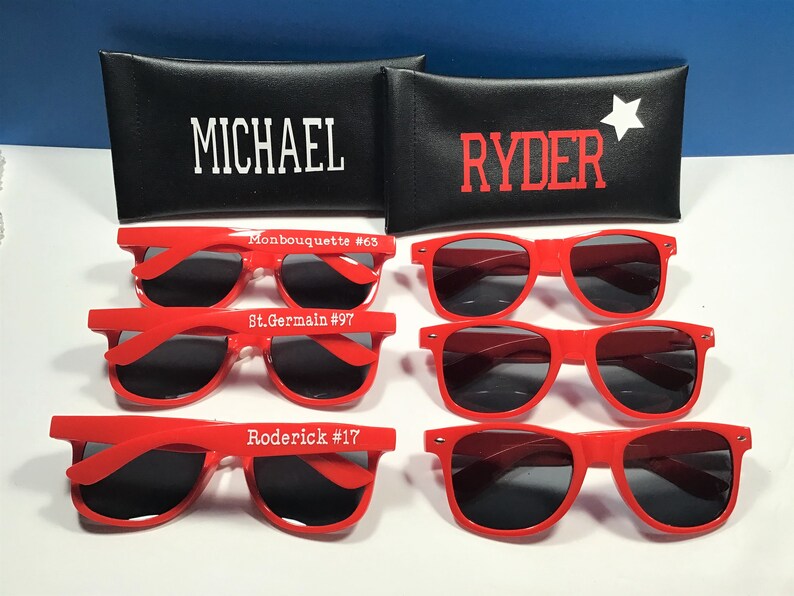 May include: Red sunglasses with dark lenses are displayed, some with names and numbers printed on the frames. Two black cases are visible, one with "MICHAEL" and the other with "RYDER" and a white star.