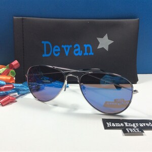 May include: Silver aviator sunglasses with blue mirrored lenses in a black case with the name "Devan" and a star printed on it. The sunglasses come with a free name engraved tag.