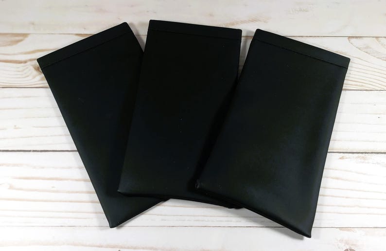 May include: Three black fabric placemats, folded and stacked on a white wooden surface.