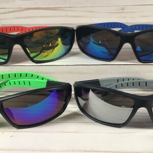 May include: Four pairs of black sunglasses with different colored lenses and frames. The lenses are mirrored and the frames have a rubberized texture. The sunglasses are arranged in two rows of two.