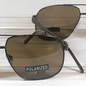 May include: Two pairs of brown polarized sunglasses with a black metal frame. The sunglasses have a square shape and the lenses are tinted brown.
