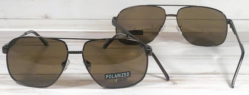 May include: Two pairs of brown polarized sunglasses with a black metal frame. The sunglasses have a square shape and the lenses are tinted brown.