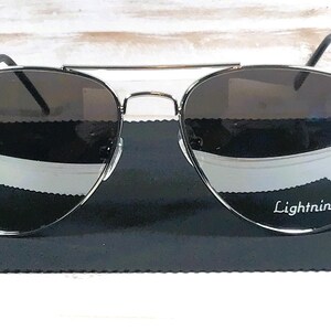 May include: Aviator-style sunglasses with dark lenses and a silver frame. The sunglasses rest on a black microfiber cloth. The text "Lightning" is printed on the lens.