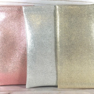 Puede incluir: Tres estuches rectangulares para gafas en fila. Los estuches son en tonos rosa, plateado y dorado. Cada estuche tiene un patr&oacute;n texturizado y punteado. Los estuches est&aacute;n hechos de un material brillante y est&aacute;n de pie.
